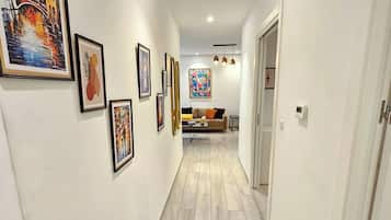 A hallway with a wooden floor, white walls, and several framed artworks.