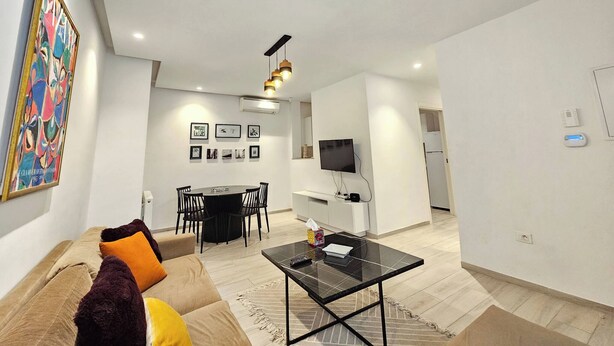 A modern living room with a sofa, coffee table, and a dining area with chairs and a table. - Contemporary Haven in the Heart of La Marsa (La Marsa)