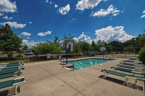 Ein Poolbereich mit Basketballkörben, grünen Bänken und blauem Himmel.