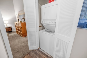 A laundry room with a dryer and washing machine, wooden dresser, and a lamp.