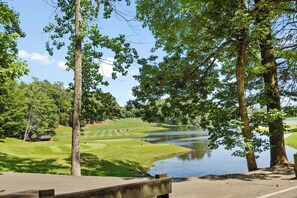 A golf course with a water body, trees, and a concrete viewing platform.