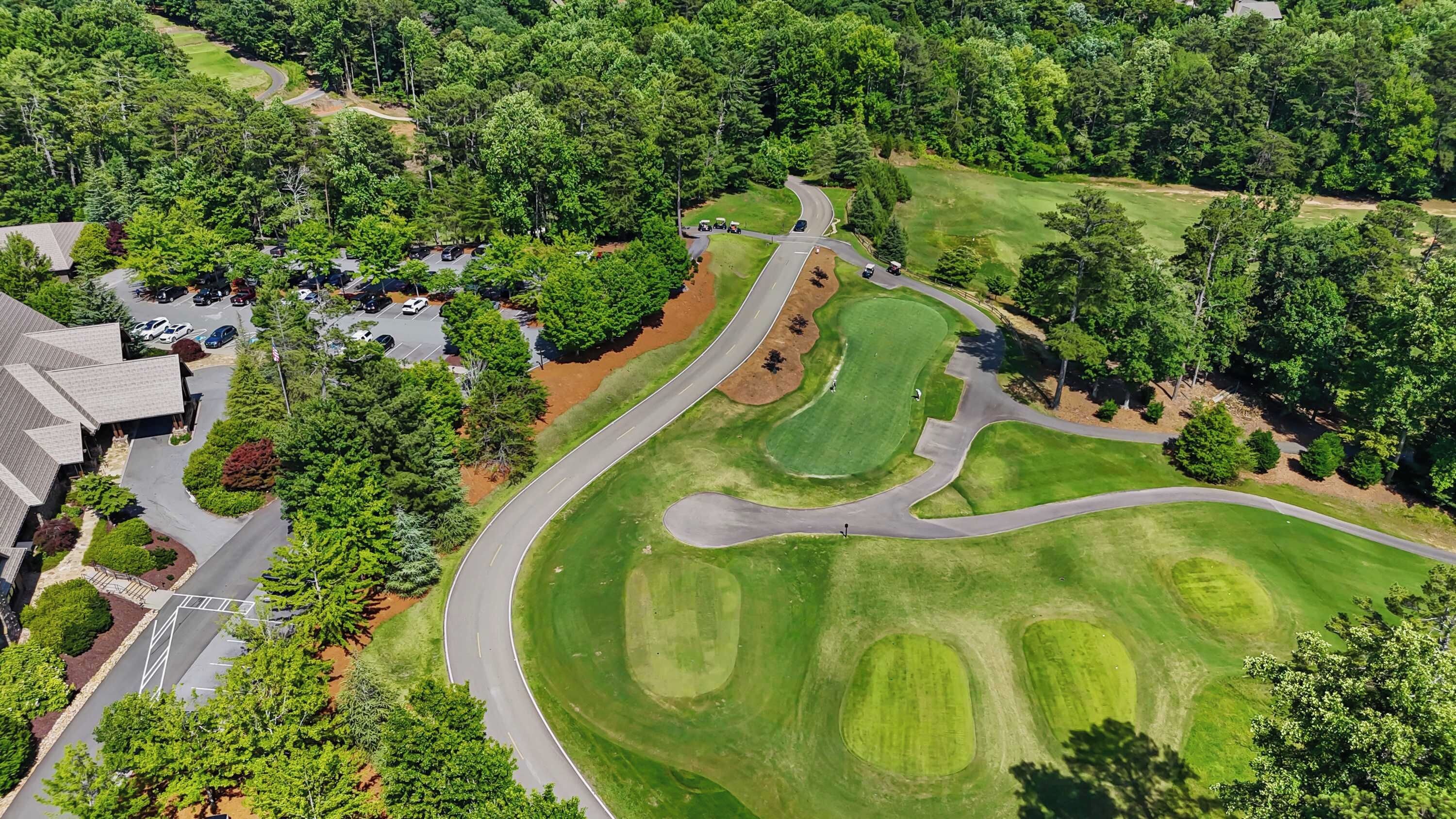 An aerial view of a golf course with a winding road, parking areas, and residential buildings.