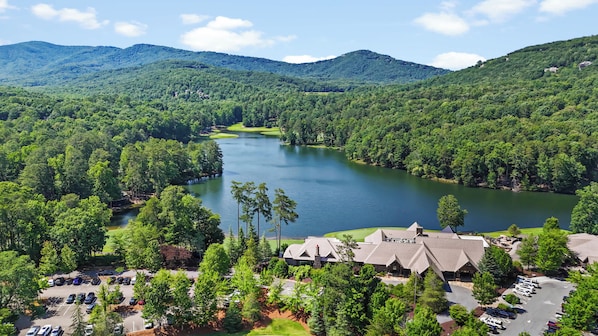 A resort with a lake, surrounded by forested hills, featuring a parking lot and multiple buildings.