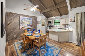 A dining area with a wooden table set for four, a ceiling fan, and a kitchen in the background. - The Chestnut Hideaway - Big Canoe Resort (Jasper)