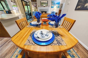 A dining table set with blue tableware, surrounded by wooden chairs, in a room with a fireplace and a bookshelf.