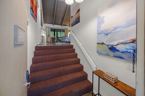 A staircase with a patterned carpet, a wooden table with a geometric object, and a large abstract painting on the wall.