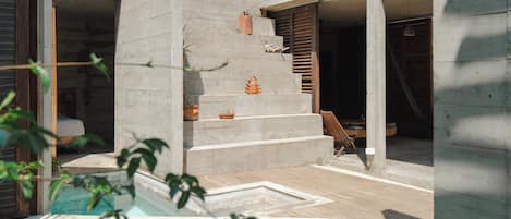 A modern architectural structure with concrete walls, a wooden deck, and a staircase leading to an interior space.