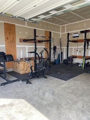 A garage with a stationary bike, weightlifting equipment, and a bench.