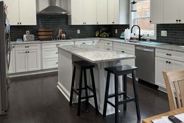 A modern kitchen with white cabinets, a marble island, and black stools.