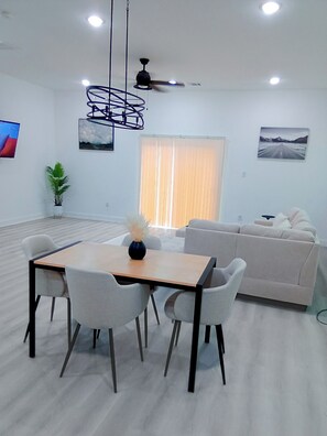 A modern living room with a dining area, a ceiling fan, and a large window with blinds. - Cherry Lux (Houston)