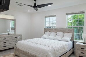A bedroom with a bed, bedside tables, a ceiling fan, and windows. - Cherry Lux (Houston)