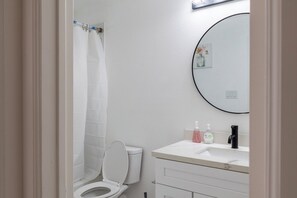 A bathroom with a toilet, a sink with soap dispensers, and a shower curtain. - Cherry Lux (Houston)