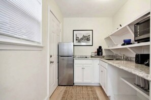 A compact kitchen with white cabinetry, a stainless steel refrigerator, a microwave, and a sink. - Pink Cottage: Uptown Studio + Easy Parking + Courtyard (New Orleans)