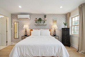 A bedroom with a large bed, two bedside tables with lamps, a dresser, a mirror, and a window with curtains. - Pink Cottage: Uptown Studio + Easy Parking + Courtyard (New Orleans)