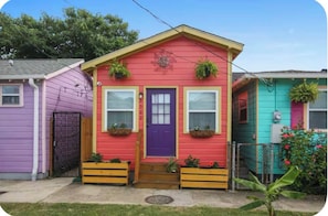 A colorful house with a purple door, two windows, and a small porch area with planters. - Pink Cottage: Uptown Studio + Easy Parking + Courtyard (New Orleans)