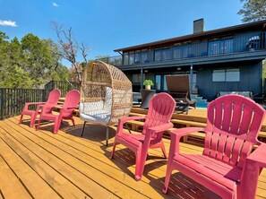 A wooden deck with red Adirondack chairs and a wicker swing chair. - Lakeside 4BR w Pool, Hot Tub, Dock, B-ball Court (Leander)