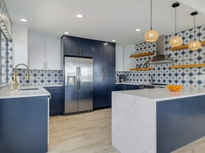 A modern kitchen with a central island, dark cabinetry, and patterned backsplash. - Lakeside 4BR w Pool, Hot Tub, Dock, B-ball Court (Leander)
