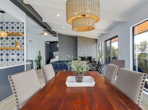 A dining area with a wooden table, cushioned chairs, and a hanging light fixture. - Lakeside 4BR w Pool, Hot Tub, Dock, B-ball Court (Leander)