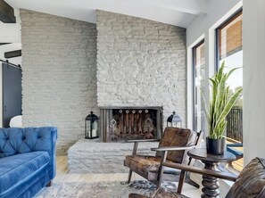 A living room with a stone wall, a fireplace, a blue sofa, and a potted plant. - Lakeside 4BR w Pool, Hot Tub, Dock, B-ball Court (Leander)