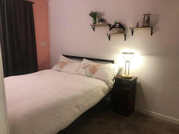 A bedroom with a bed, a bedside lamp, and two wall-mounted shelves with decorative items.