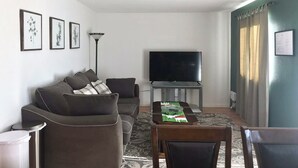 Un salon comprenant un ensemble de canapés, un téléviseur à écran plat, une table à manger avec des chaises et un tapis à motifs.