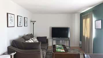 Un salon comprenant un ensemble de canapés, un téléviseur à écran plat, une table à manger avec des chaises et un tapis à motifs.