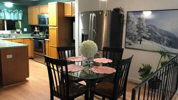 A modern kitchen with wooden cabinets, stainless steel appliances, and a dining area with a glass table and chairs.