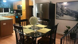Une cuisine moderne avec des meubles en bois, un réfrigérateur et un coin repas comprenant une table et des chaises en verre.