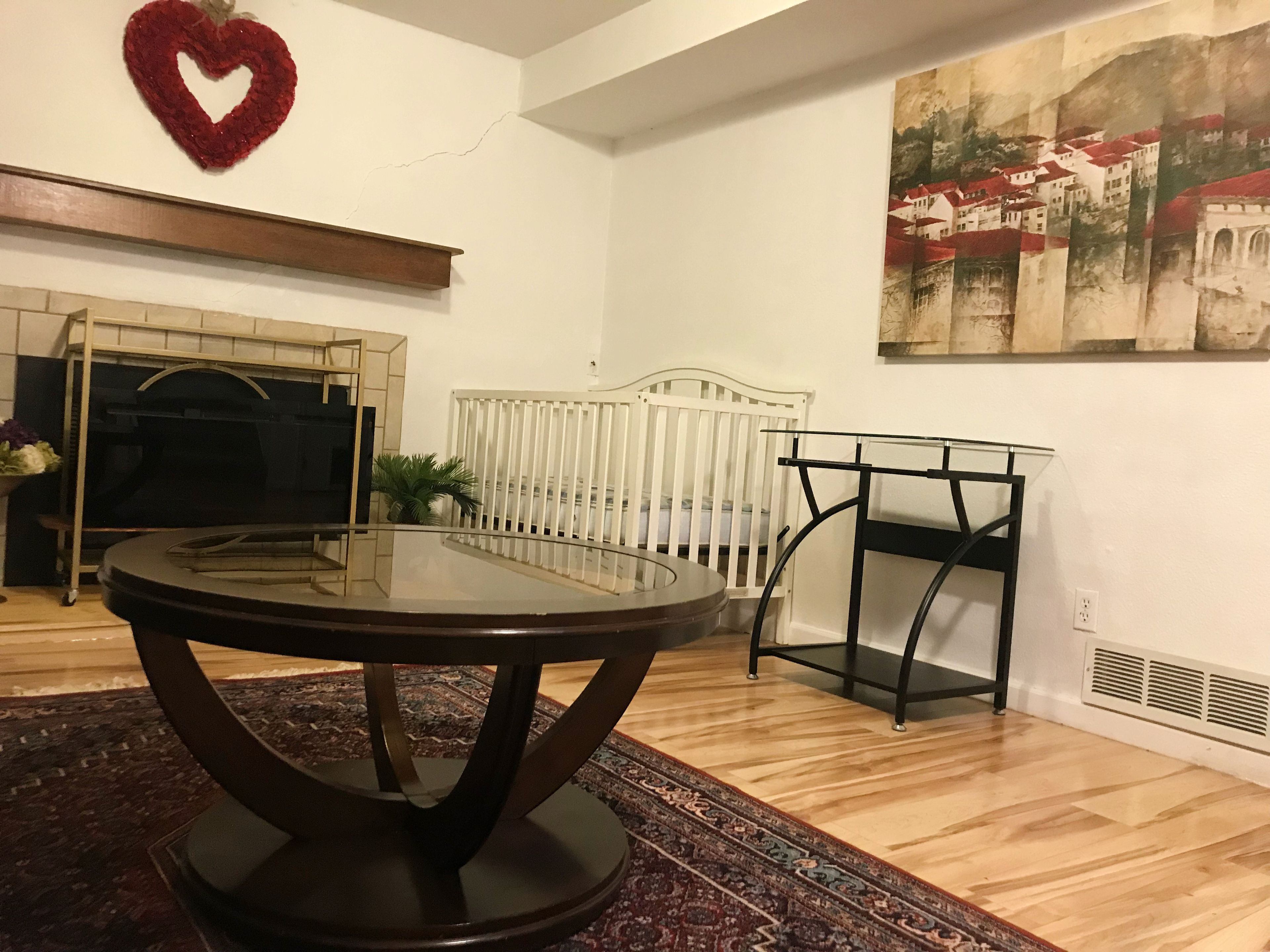 Une pièce avec une table ronde, un berceau blanc, une cheminée et un tableau au mur.