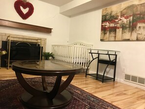 A room with a round table, a white crib, a fireplace, and a painting on the wall.