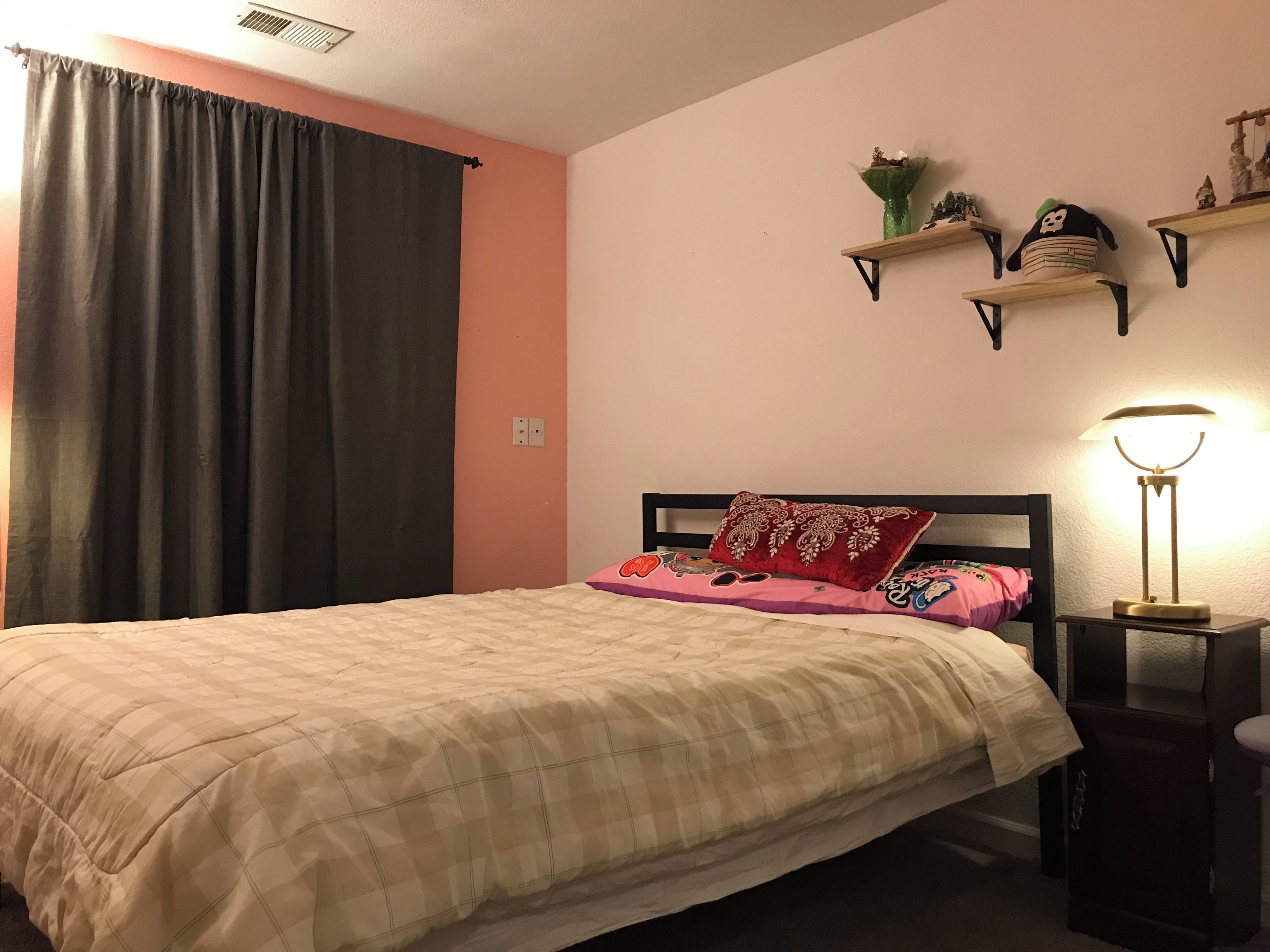 Una camera da letto con un letto, un comodino, una lampada, una finestra con tende e mensole a parete.