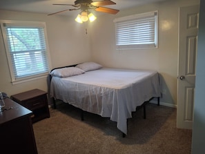 A bedroom with a single bed, a nightstand, a ceiling fan, and two windows with blinds.