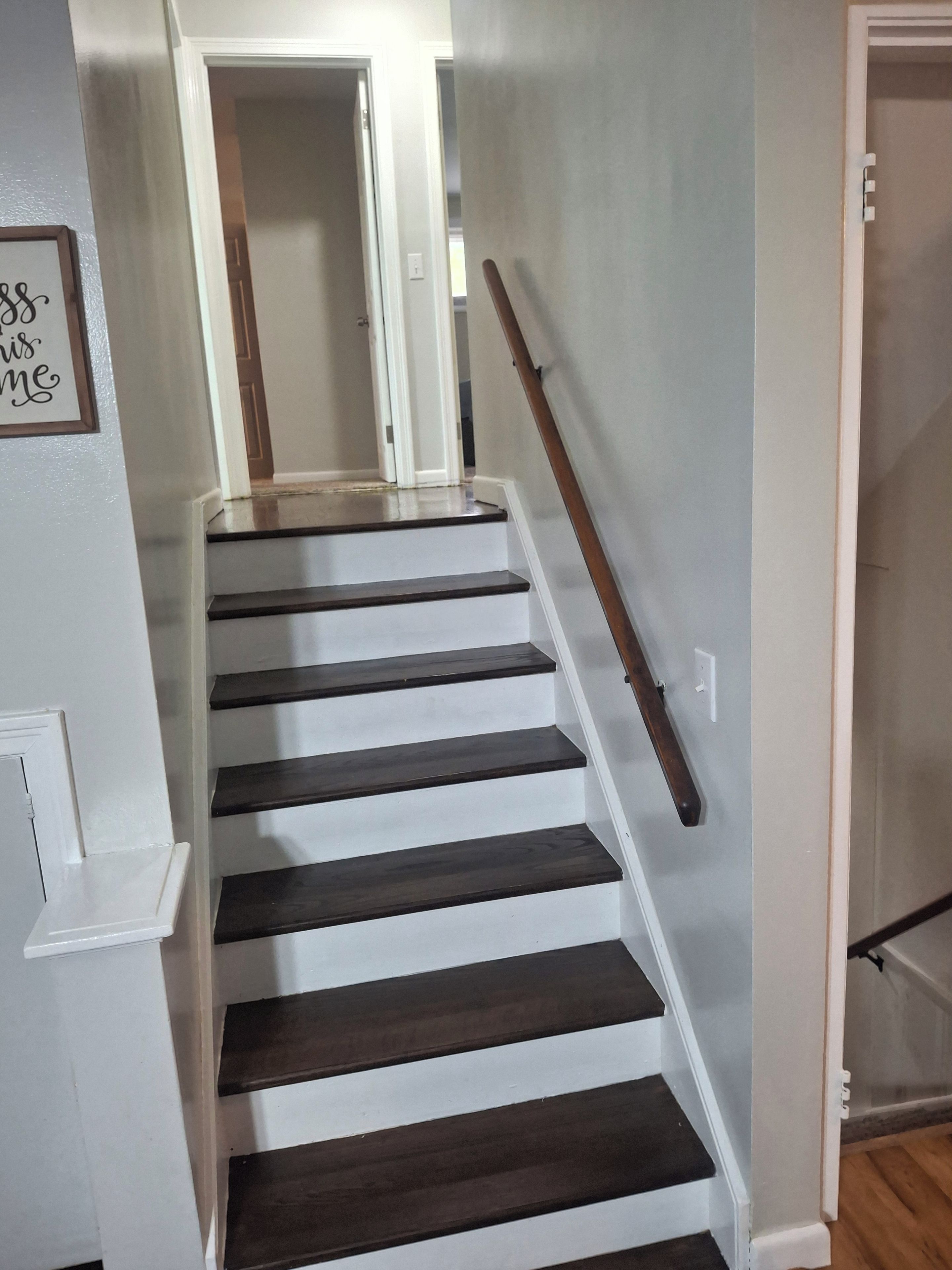 A staircase with dark wooden steps and a white handrail, leading to an interior space.