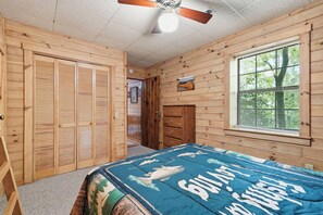 A bedroom with a bed, a window with blinds, a ceiling fan, and wooden walls.