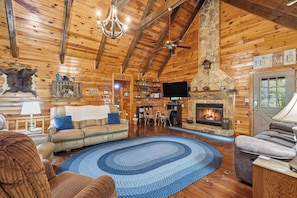 A log cabin interior with a fireplace, wooden walls, a chandelier, and a cozy seating area.
