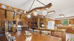 Um interior rústico de madeira com uma grande mesa de jantar, armários de madeira e uma lareira de pedra.
