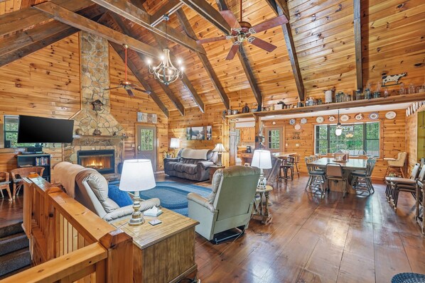 A spacious log cabin interior with a fireplace, a television, a dining area, and a cozy seating area.