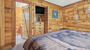 Quarto com painéis de madeira, uma cama, uma televisão e um guarda-roupa.