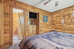 Una stanza con rivestimento in legno, un letto, una televisione e un armadio.