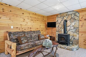 A cozy cabin interior with a wooden sofa, a stone fireplace, and a television mounted on the wall.