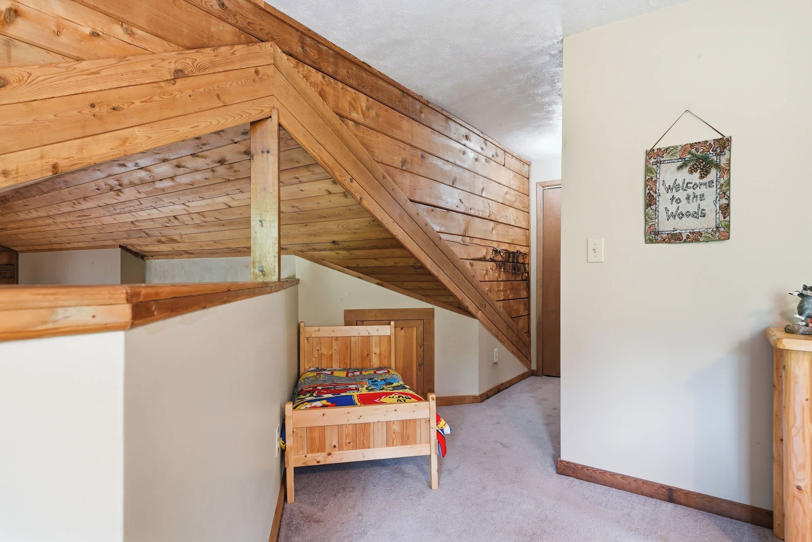 Ein Schlafzimmer mit schräg stehender Decke, einem hölzernen Bett und einem Willkommensschild an der Wand.