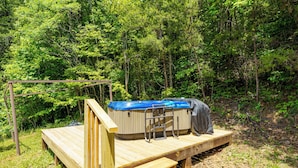 A wooden deck with a hot tub and a covered area, surrounded by dense forest. - LeVasseur Cabin  Simple Escape (Murphy)