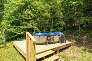 Eine Holzterrasse mit Whirlpool und Überdachung, umgeben von dichtem Wald.