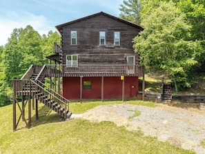 A two-story wooden cabin with a red door and a wooden staircase leading to a balcony.