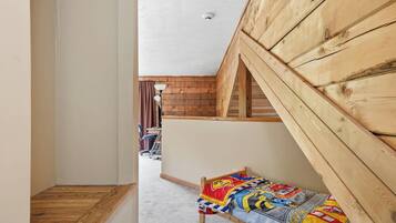 Ein schmaler Flur, der zu einem Schlafzimmer mit geneigter Decke und Holzwänden führt.