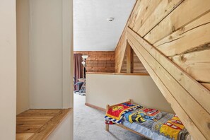 A narrow hallway leading to a bedroom with a sloped ceiling and wooden walls.