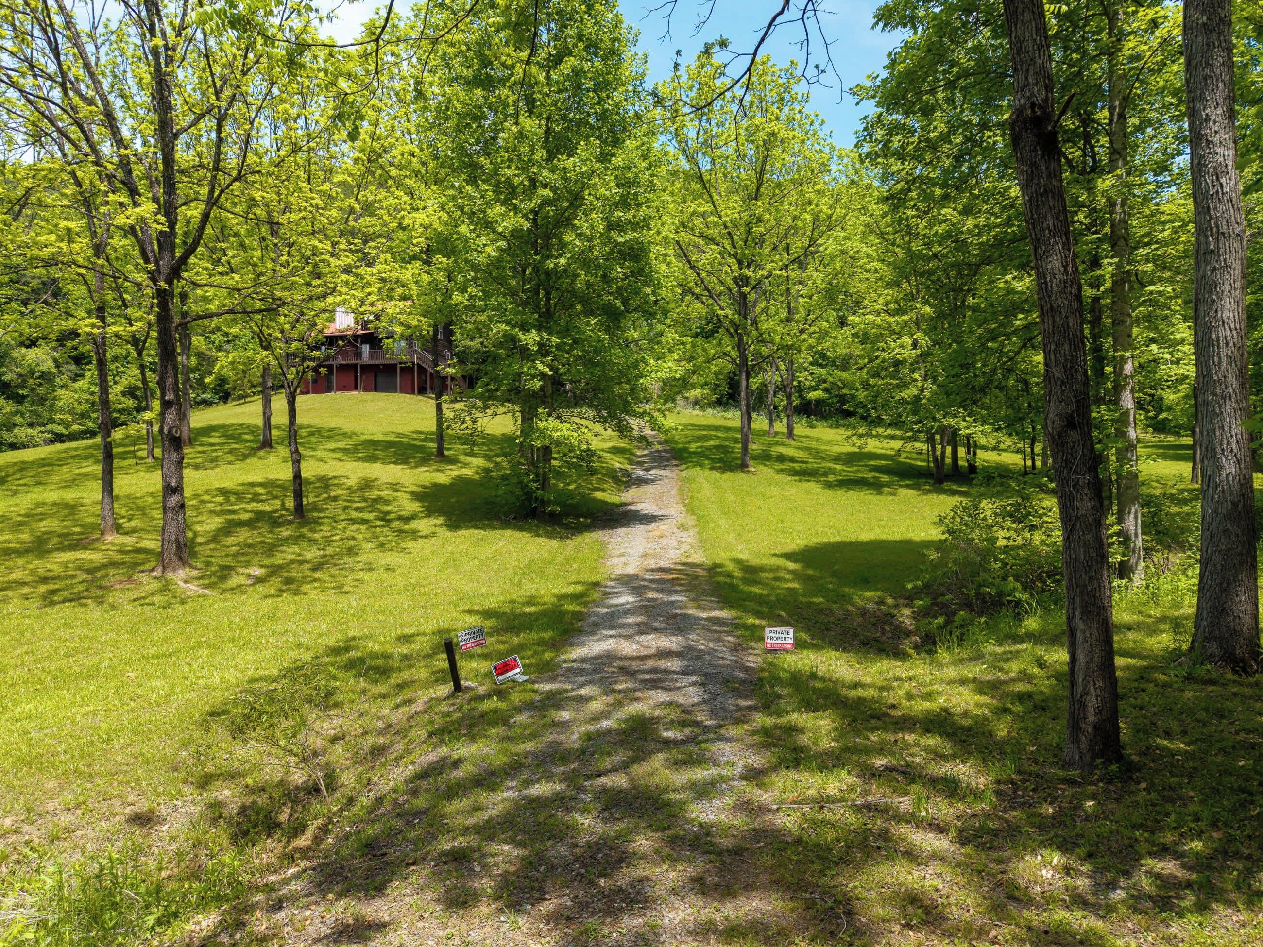 Un chemin menant à une propriété avec un bâtiment rouge, entouré d’arbres et d’herbe.