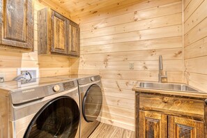 Ein kleiner Waschbereich mit einer Samsung Waschmaschine und einem Trockner, Holzausbau und einem Edelstahlspülbecken.