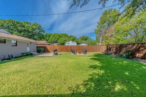 A backyard with a lawn, a wooden fence, and a barbecue grill. - Perfect 3-bedroom house w/ Smart TV, Patio, in peaceful Dallas neighborhood (Dallas)