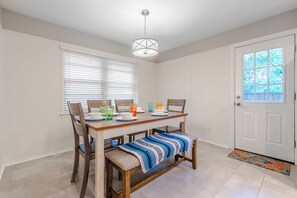 Un comedor con una mesa de madera, sillas y un banco. Hay una puerta con un ventanal y una lámpara en el techo.